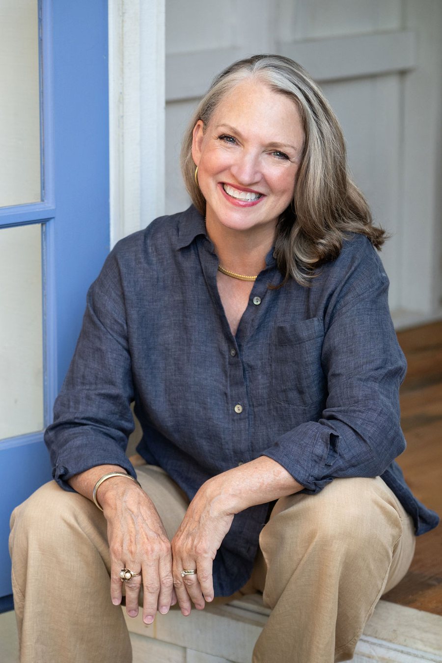 Sharon E. Reed, smiling, seated in a periwinkle-blue doorway